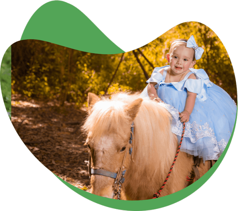 A little girl in blue dress riding on the back of a pony.